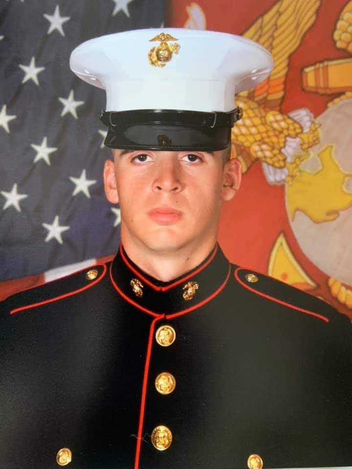 A army personal wearing full uniform and standing in front of the flag