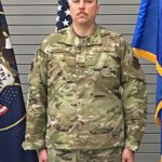 A soldier in camouflage military uniform standing indoors.